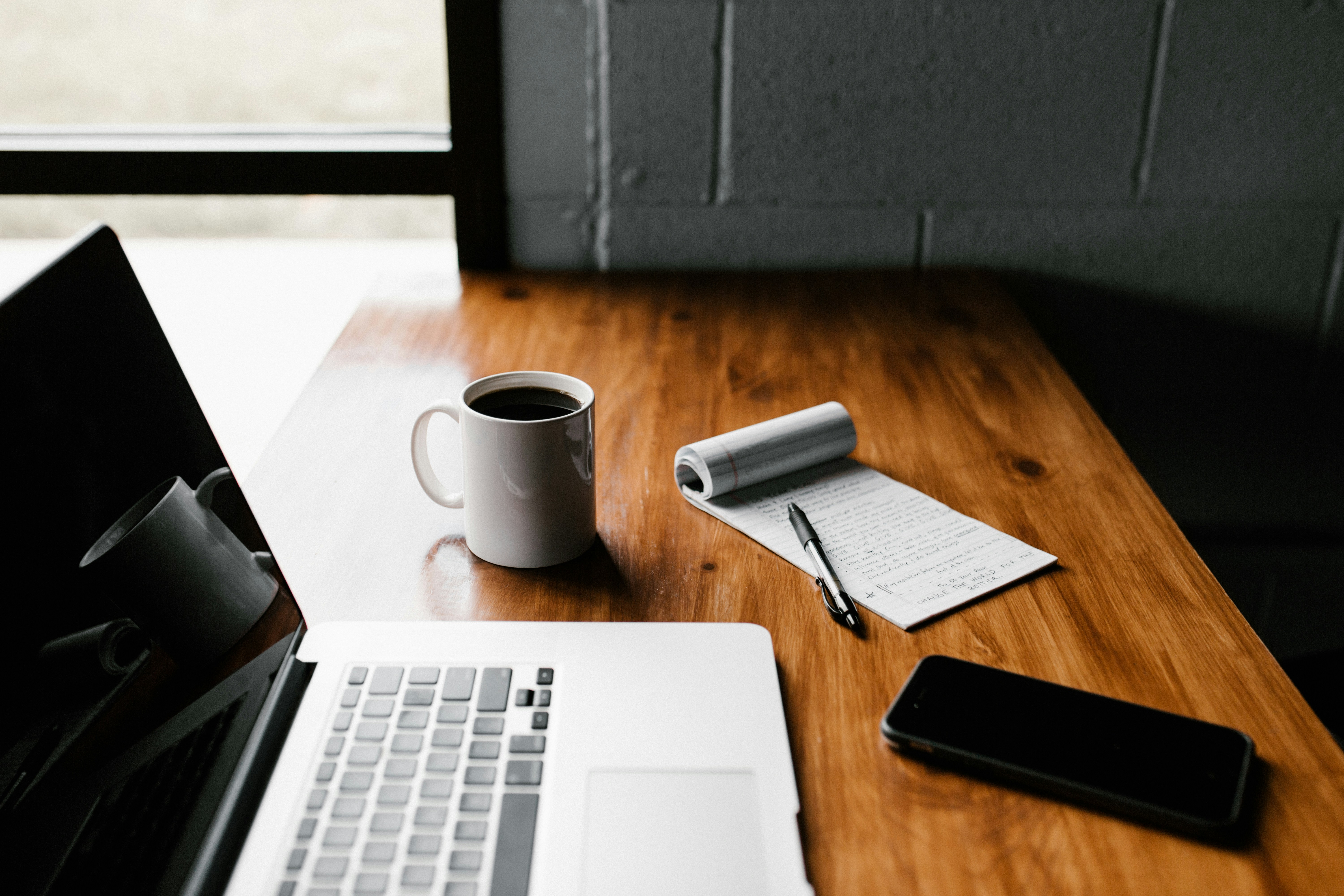 A laptop sitting on a desk next to a cup of coffee and a notepad.